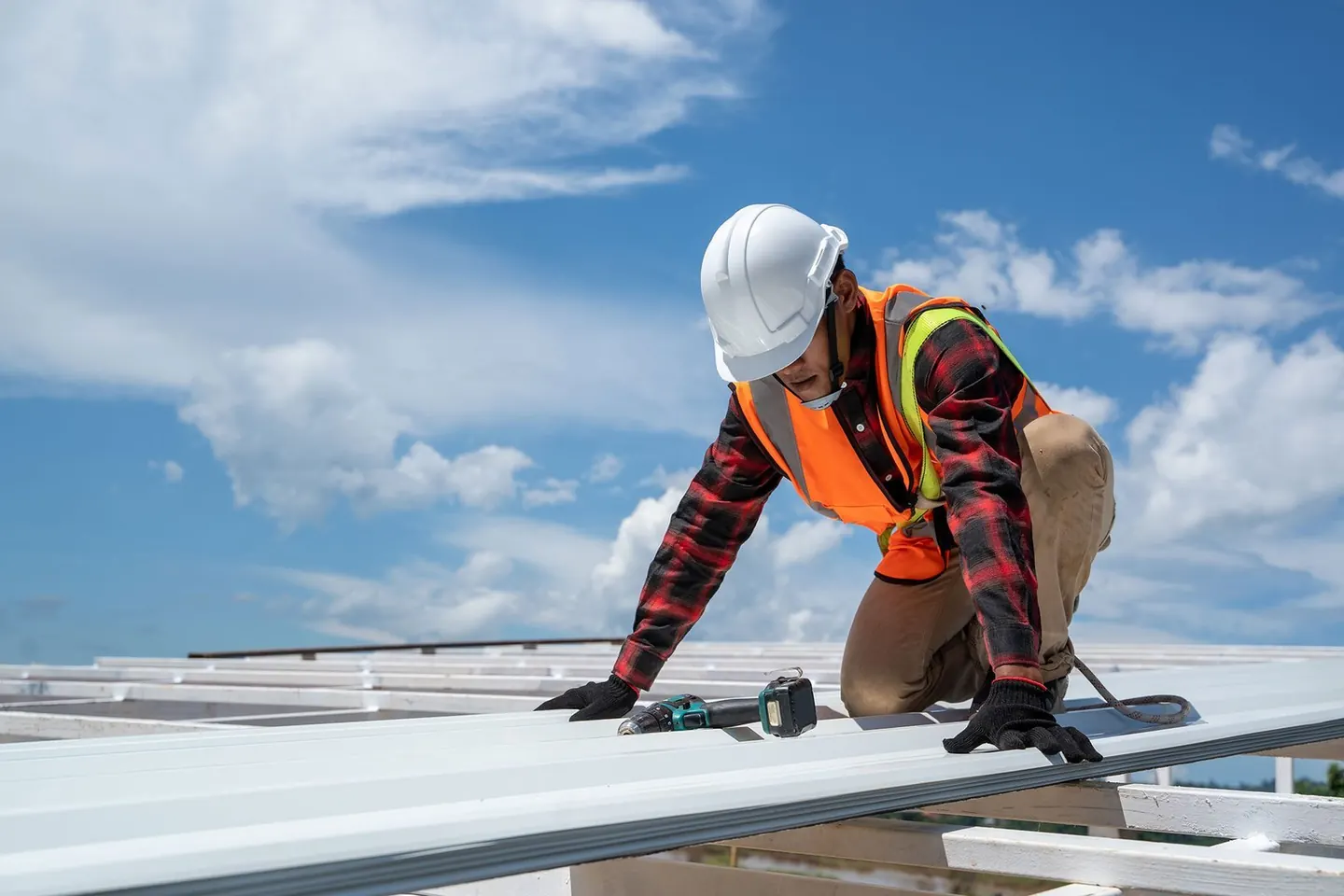 Roofer in hi-vis and gloves fixing new pale steel roof sheets